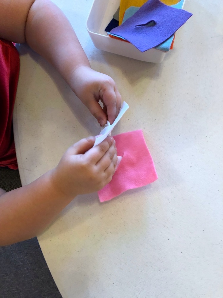 Fine motor practice: pulling buttons through a slit of fabric.